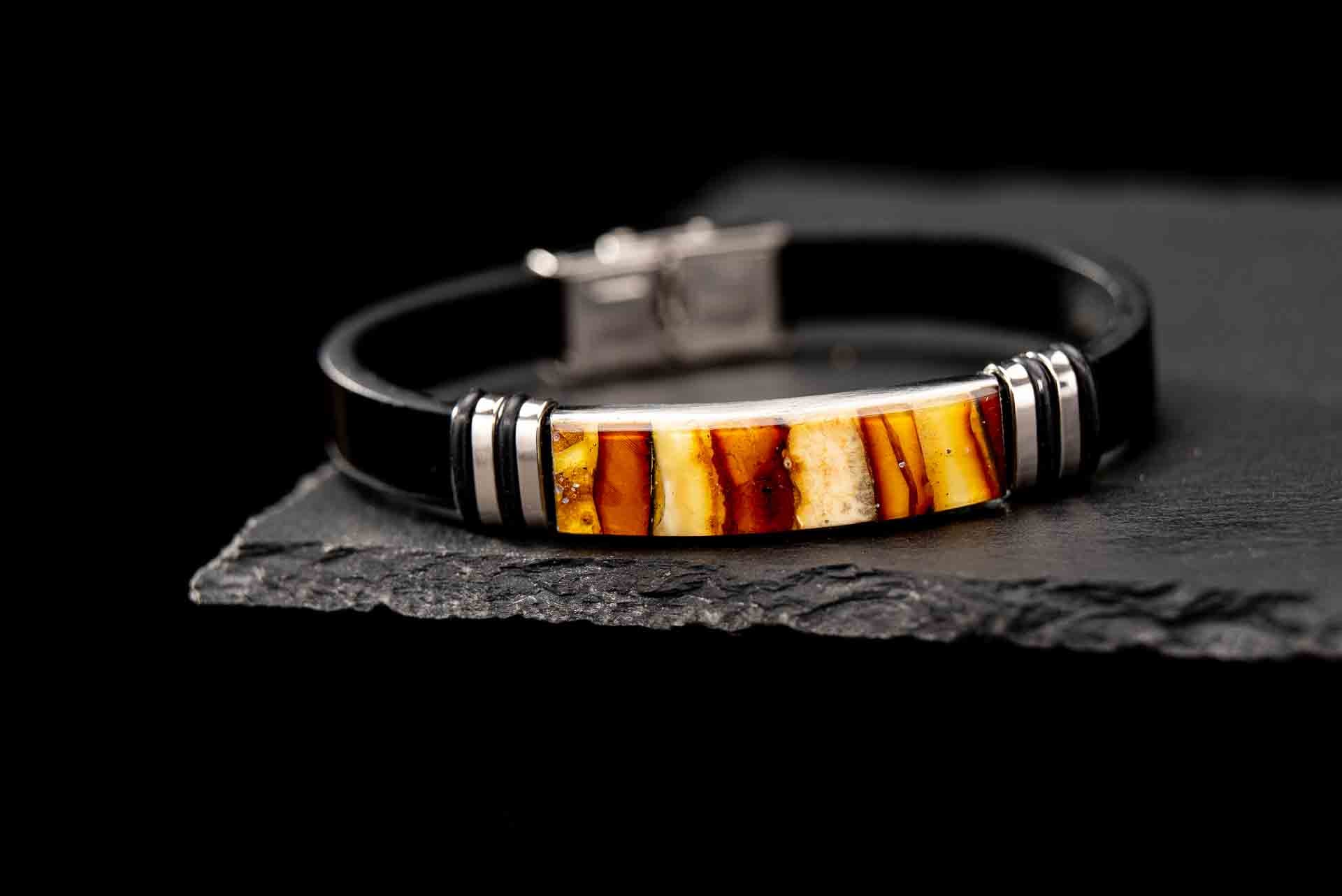 Handcrafted black genuine leather bracelet with real Baltic amber mosaic inlay centerpiece. Luxury unisex jewelry featuring silver-tone accents and secure lobster clasp, displayed on dark slate stone β premium amber bracelet for men and women.