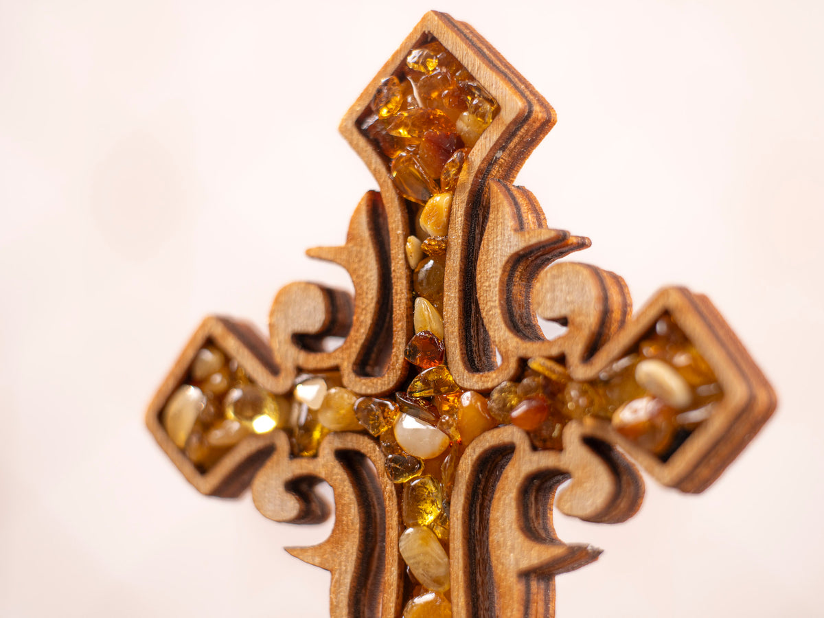 Close-up of the upper section of the standing wooden cross, showing amber pieces in varied tones and ornate wood cutouts.