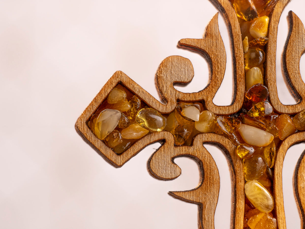 Close-up of the centre and side of the wooden cross with amber pieces in varied tones and ornate wood cutouts.