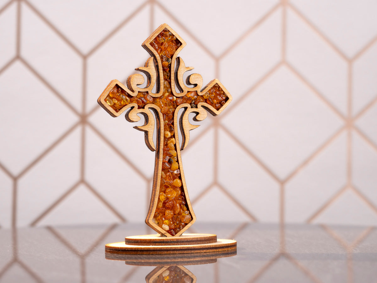 Standing wooden cross with amber pieces in the ornate front panel on an oval base, front view.