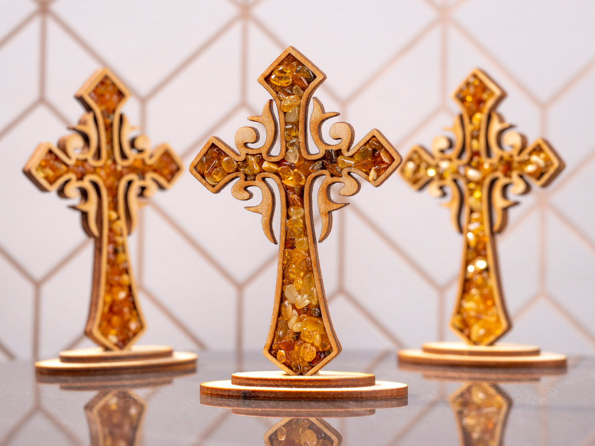 Three standing wooden crosses with amber pieces, with the centre cross in focus and two crosses in the background.
