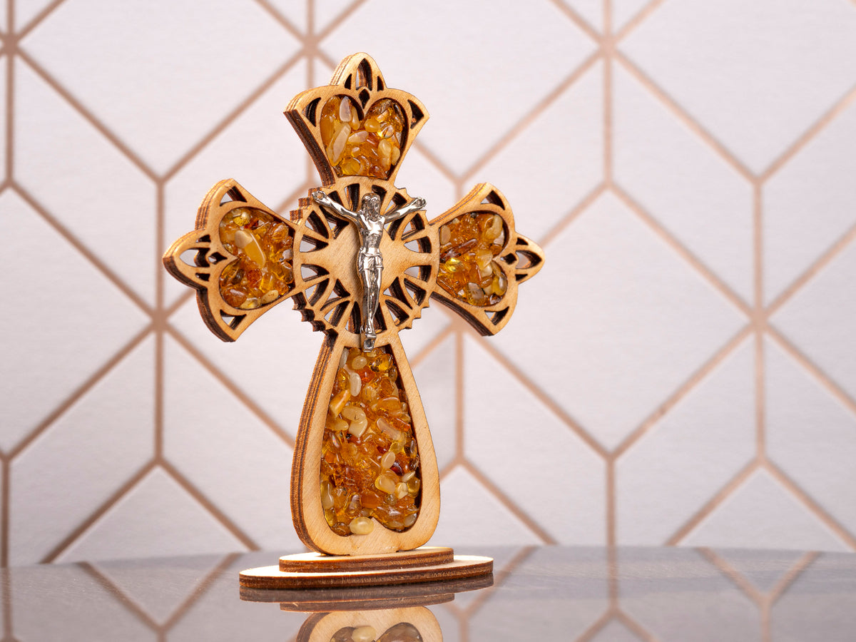 Standing wooden cross with cherry-toned Baltic amber pieces and a silver-coloured crucifix figure, front view.
