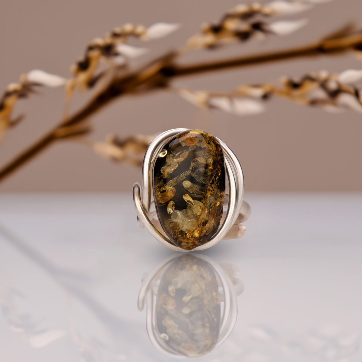 Front view of the adjustable amber ring with an elongated dark cabochon wrapped by a silver-toned metal band