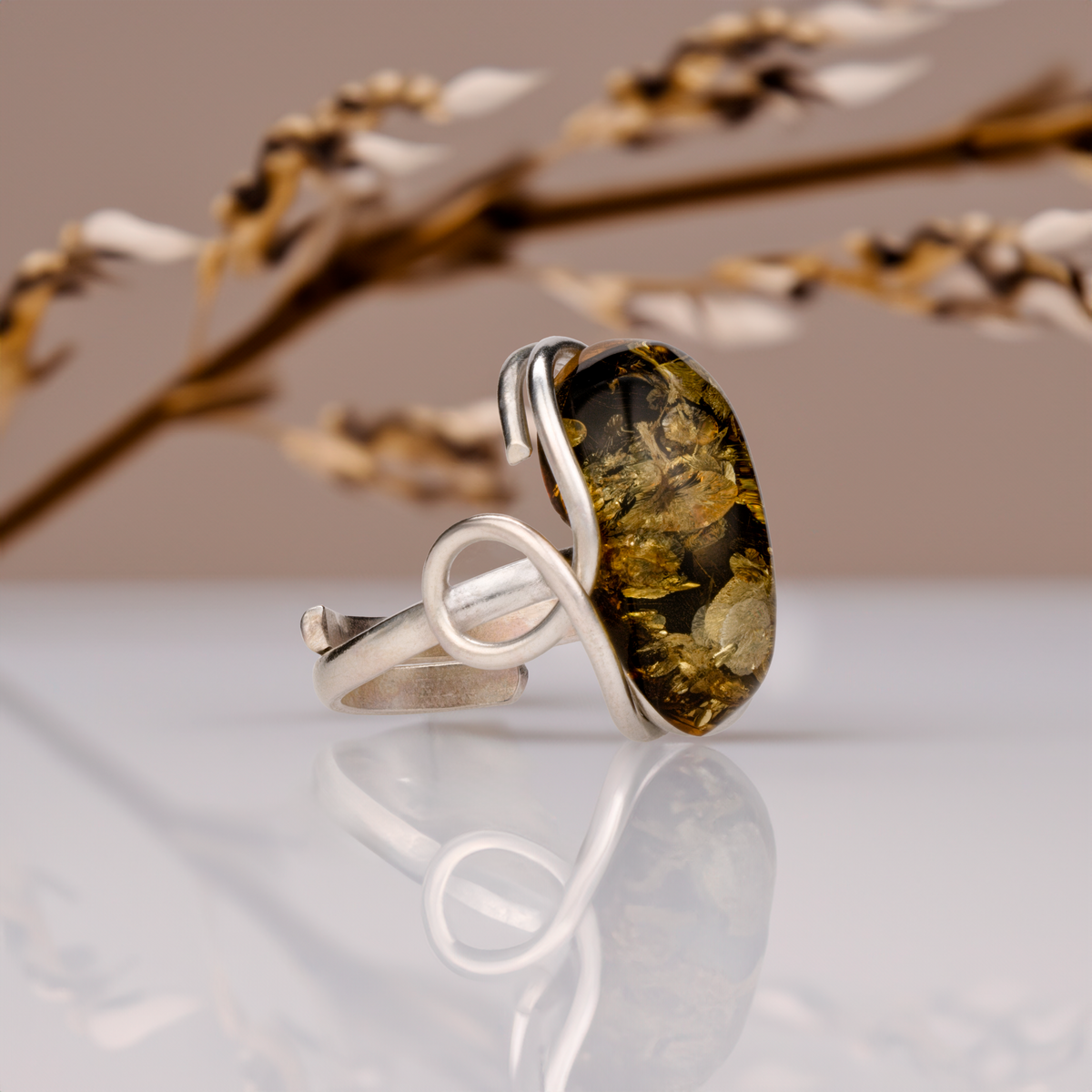 Side view of the adjustable amber ring with an elongated dark cognac-toned cabochon and curved silver-toned metal band