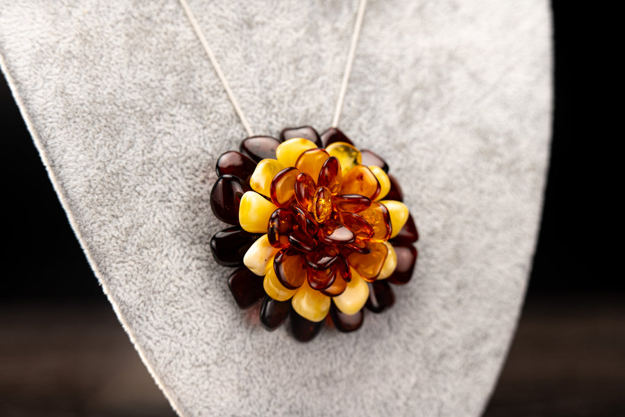 Amber flower brooch and pendant on a pale cord, displayed on a grey jewellery stand.