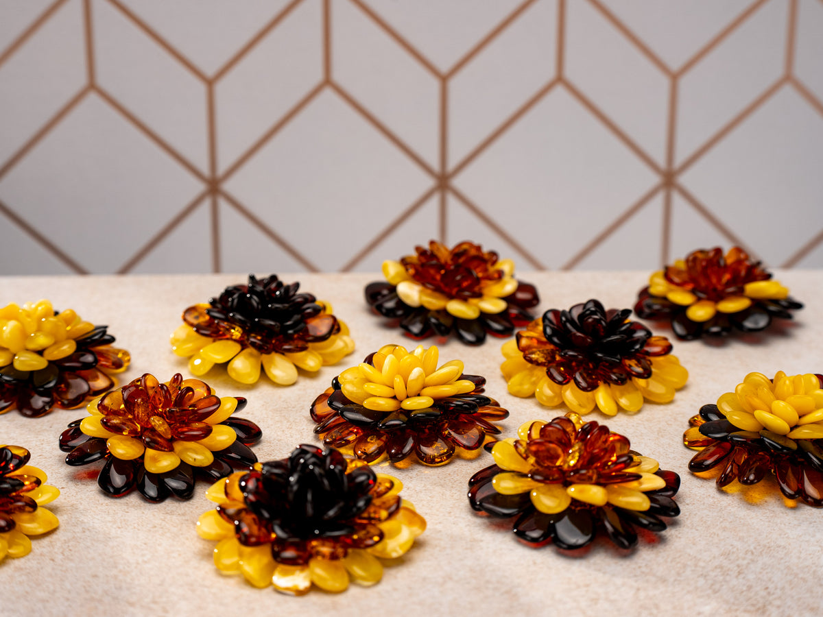 Amber flower brooches and pendants in yellow, cognac and dark tones arranged on a light surface.