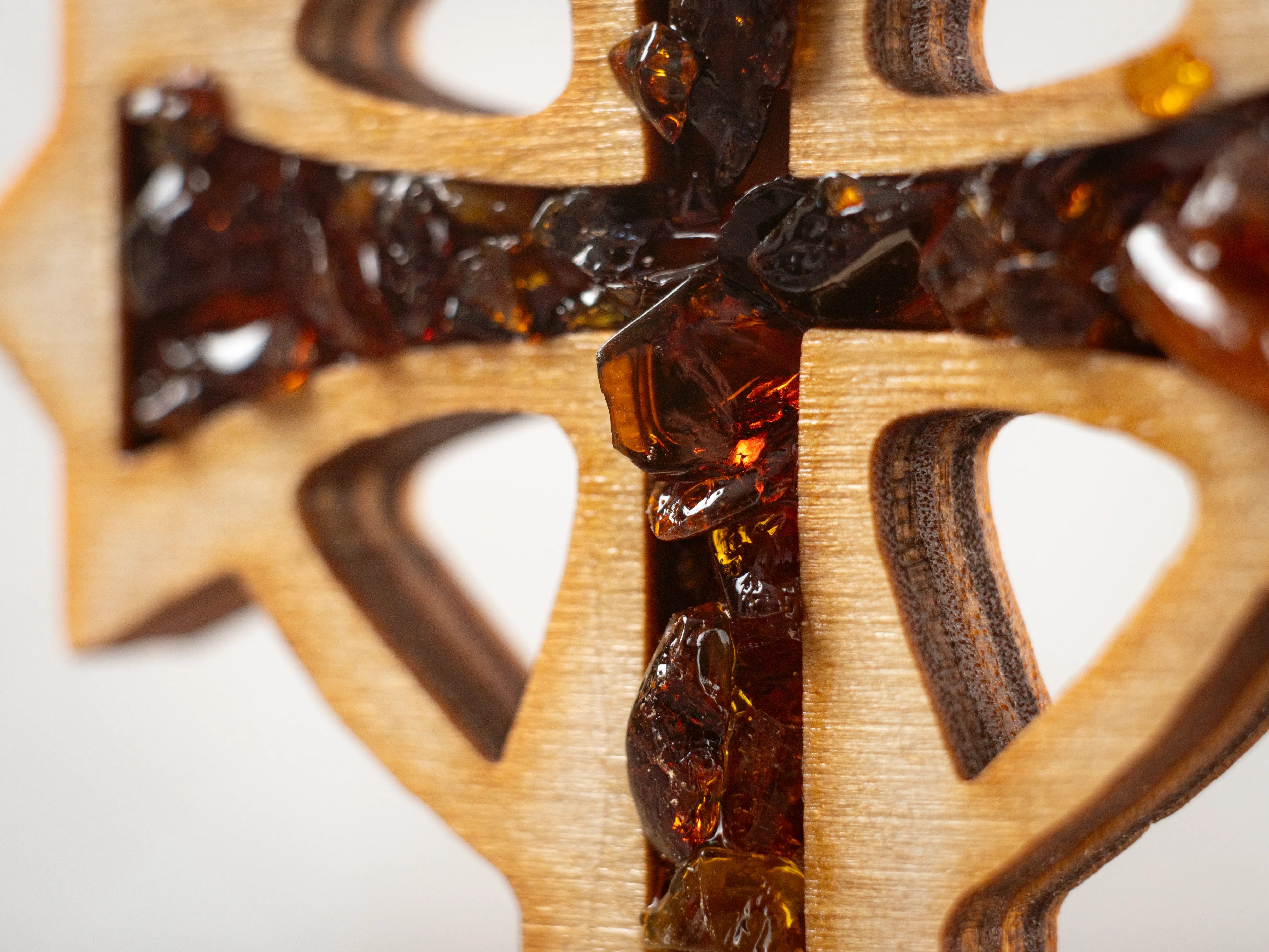 Macro close-up of BalticBliss genuine amber cross showing rich cognac Baltic amber chips set in layered birch wood, authentic Lithuanian handmade religious décor detail, real Baltic amber art for spiritual home gifts.