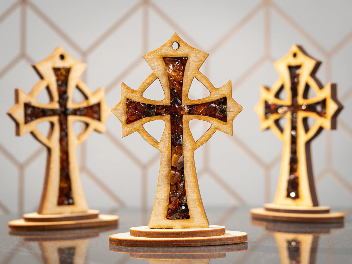 Three standing wooden crosses with amber pieces, with the centre cross in focus and two front-facing crosses in the background.