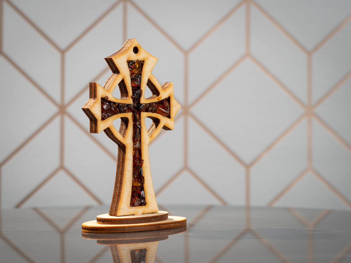 Standing wooden cross with dark-toned amber pieces in the front panel on a layered oval base, front view.