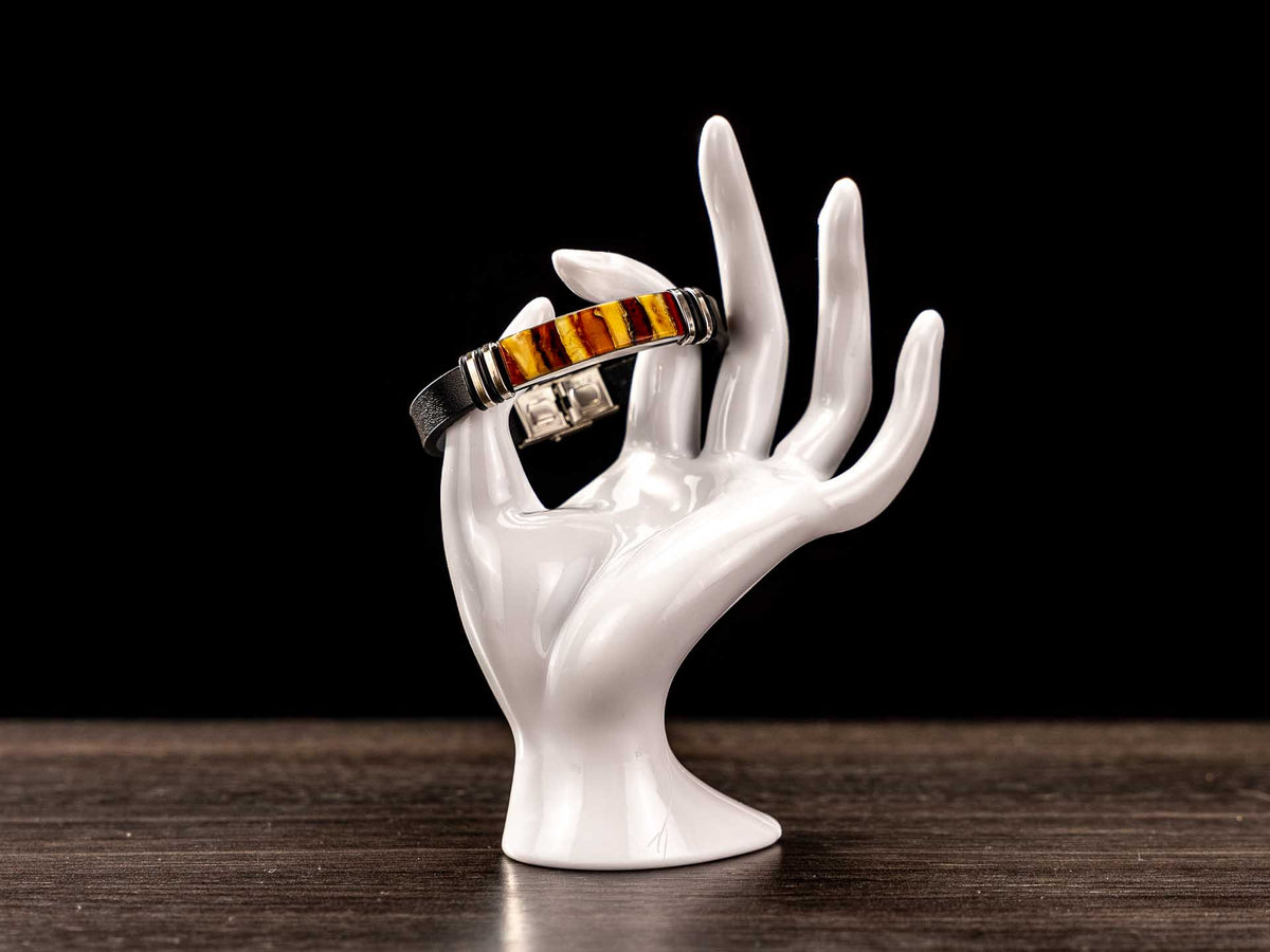 Handcrafted black genuine leather bracelet with real Baltic amber mosaic centerpiece displayed on white ceramic hand mannequin. Luxury unisex amber jewelry showing perfect fit, silver-tone accents and secure clasp – premium wearable amber bracelet.