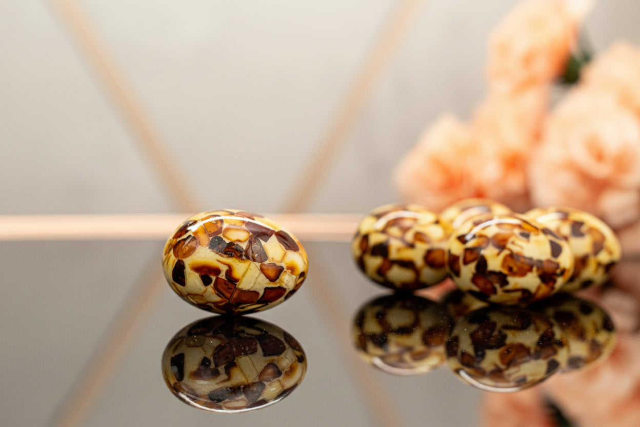 Luxury handcrafted amber mosaic Easter egg made with genuine natural amber pieces. Elegant lifestyle shot on reflective mirror surface with soft peach flowers in background – exclusive Easter home decor.