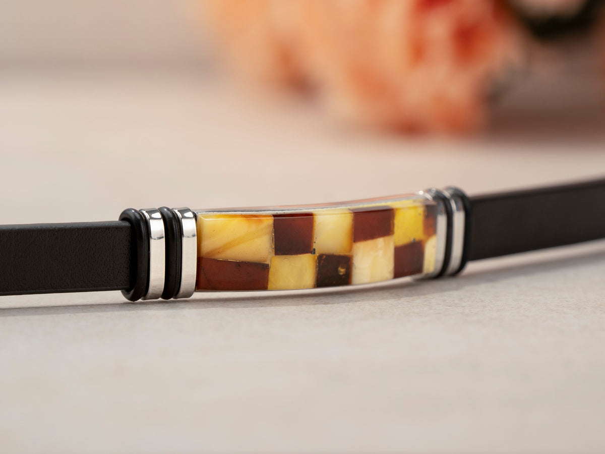 Macro close-up of handcrafted real Baltic amber mosaic inlay on black leather bracelet. Individual natural amber pieces arranged in a rich checkerboard pattern within polished silver-tone setting – showcasing artisanal amber jewelry craftsmanship.