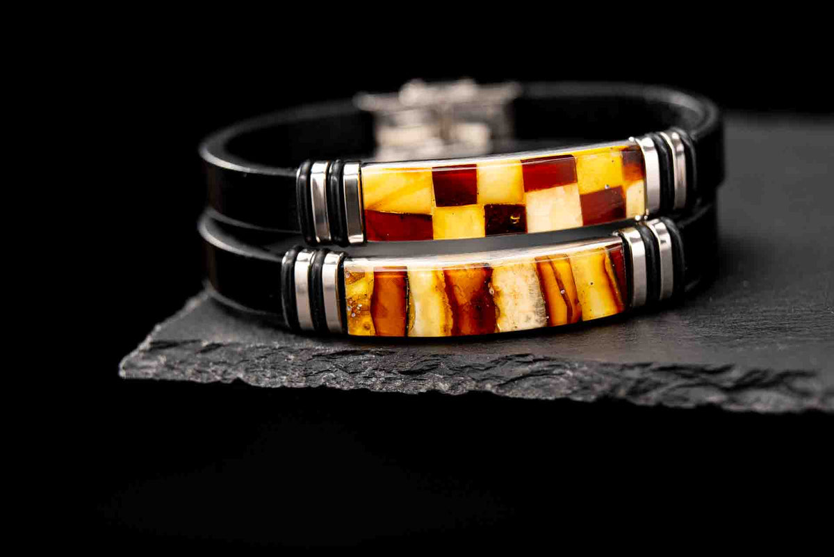 Two handcrafted black leather amber mosaic bracelets stacked on dark slate stone – luxury unisex jewelry pair with genuine Baltic amber inlays.